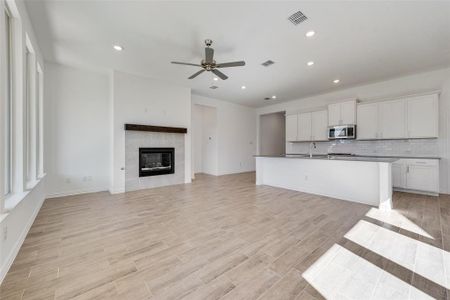 Kitchen with a tiled fireplace, ceiling fan, an island with sink, white cabinetry, and light wood-type flooring