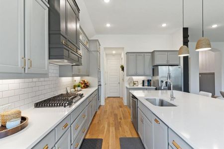 Kitchen with gray cabinets, light hardwood / wood-style flooring, decorative light fixtures, stainless steel appliances, and sink