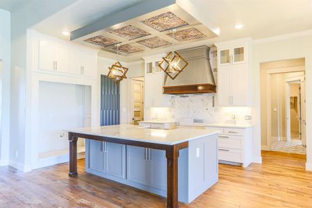 Kitchen with premium range hood, pendant lighting, white cabinetry, light hardwood / wood-style floors, and a center island