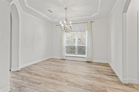 Unfurnished room featuring light wood-type flooring, a tray ceiling, a chandelier, and crown molding