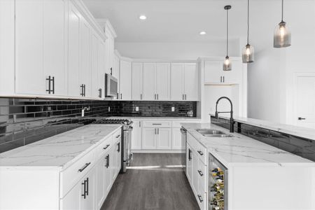 This is a modern kitchen featuring white cabinetry, marble countertops, stainless steel appliances, a gas stove, and stylish pendant lighting. The room has a sleek, monochromatic color scheme accented by a dark tiled backsplash.