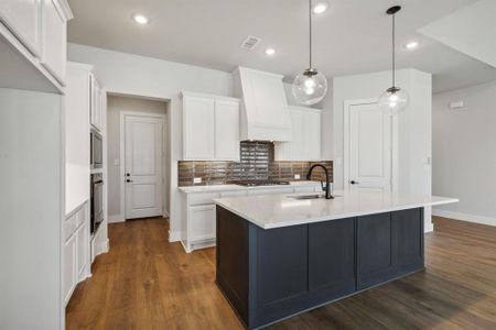 Kitchen with hanging light fixtures, oven, custom exhaust hood, dark wood-type flooring, and a center island with sink