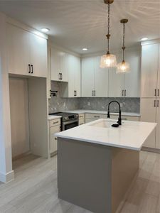 Kitchen with decorative backsplash, a kitchen island with sink, hanging light fixtures, sink, and range