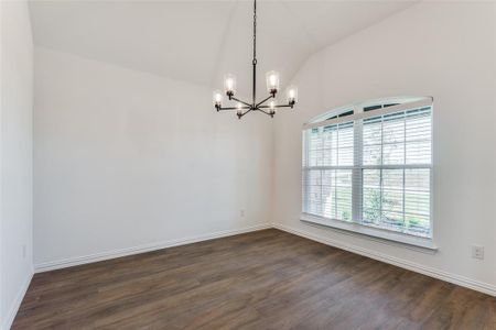 Empty room featuring vaulted ceiling, a chandelier, and dark hardwood / wood-style floors