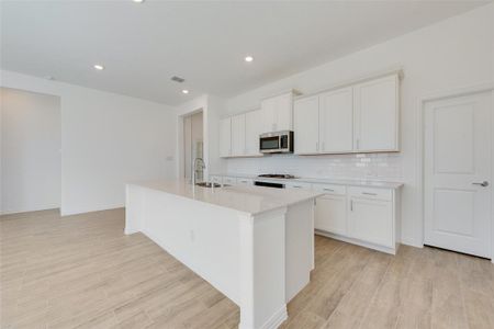 Kitchen with light hardwood / wood-style flooring, backsplash, a center island with sink, and white cabinets