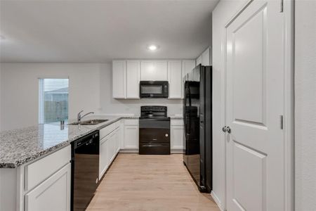 Kitchen with black appliances, white cabinets, sink, light stone counters, and light wood-type flooring
