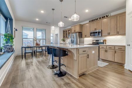 Kitchen featuring light hardwood / wood-style floors, stainless steel appliances, an island with sink, pendant lighting, and tasteful backsplash