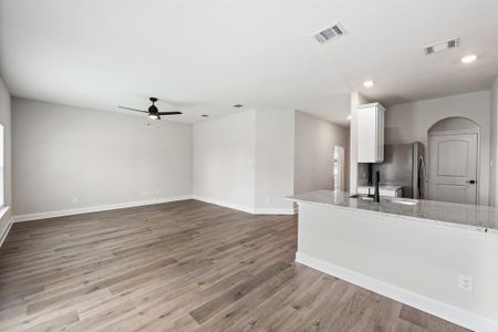 Kitchen featuring stainless steel fridge, light stone counters, light hardwood / wood-style floors, white cabinetry, and ceiling fan