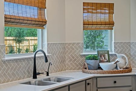 The windows brighten the beautiful kitchen space. Featured here is the spacious countertop, modern backsplash and double sink with Moen sleek kitchen faucet.