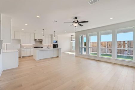 Kitchen with stainless steel oven, hanging light fixtures, white cabinetry, light hardwood / wood-style flooring, and a center island with sink