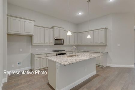 Kitchen featuring an island with sink, stainless steel appliances, decorative light fixtures, light stone counters, and light hardwood / wood-style flooring