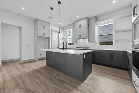 Kitchen with sink, decorative light fixtures, light hardwood / wood-style floors, decorative backsplash, and an island with sink