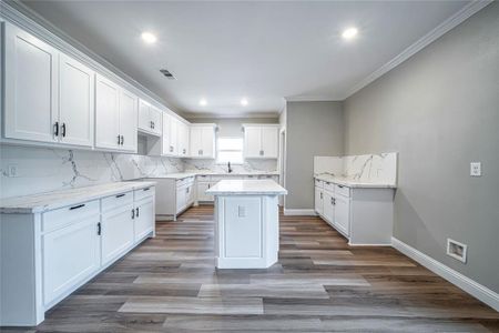 Kitchen featuring crown molding, a center island, light wood-type flooring, white cabinetry, and light stone counters