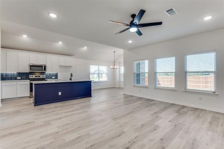 Kitchen featuring light hardwood / wood-style flooring, white cabinets, hanging light fixtures, appliances with stainless steel finishes, and a kitchen island with sink