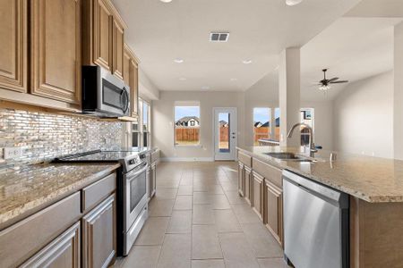 Kitchen featuring light stone countertops, appliances with stainless steel finishes, an island with sink, sink, and ceiling fan