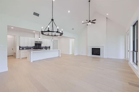 Unfurnished living room featuring sink, high vaulted ceiling, light hardwood / wood-style flooring, and ceiling fan with notable chandelier