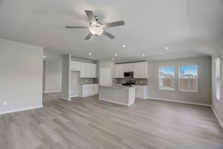 Kitchen with light hardwood / wood-style floors, white cabinets, a center island with sink, appliances with stainless steel finishes, and light stone countertops