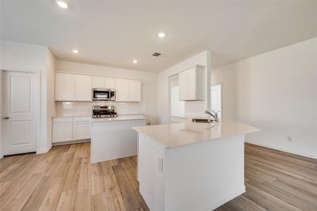 Kitchen with white cabinets, light hardwood / wood-style floors, backsplash, appliances with stainless steel finishes, and sink