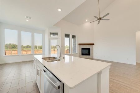 Kitchen featuring a tiled fireplace, white cabinets, sink, an island with sink, and stainless steel dishwasher