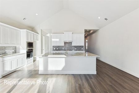 Kitchen featuring stainless steel microwave, an island with sink, backsplash, wood-type flooring, and high vaulted ceiling