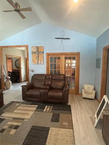 Living room with ceiling fan, light wood-type flooring, and vaulted ceiling