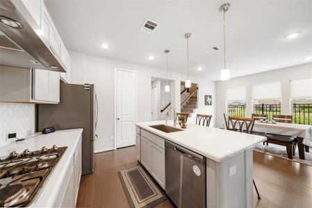 Modern, open-concept kitchen with stainless steel appliances, an island with a sink and an upgraded herringbone backsplash.  The kitchen is open into the dining area with abundant natural light and a view of the side yard with NO neighbors.