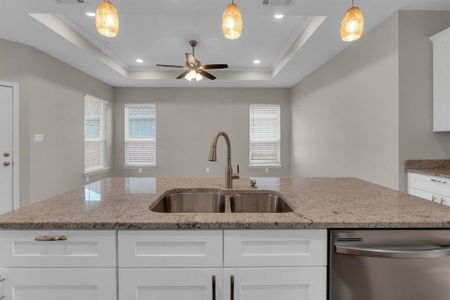 Kitchen with pendant lighting, a raised ceiling, sink, stainless steel dishwasher, and white cabinetry