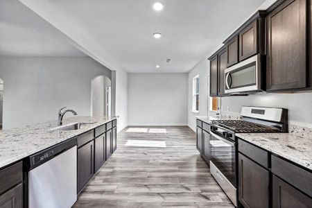 Kitchen featuring appliances with stainless steel finishes, light wood-type flooring, light stone counters, sink, and dark brown cabinetry