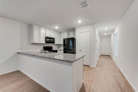 Kitchen with black appliances, white cabinets, light stone counters, and light hardwood / wood-style flooring