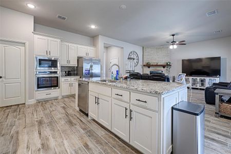 Kitchen featuring white cabinetry, ceiling fan, appliances with stainless steel finishes, and a center island with sink