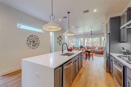 Kitchen featuring hanging light fixtures, light wood-type flooring, sink, appliances with stainless steel finishes, and a kitchen island with sink