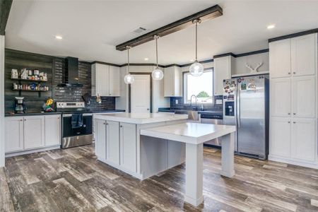 Kitchen with appliances with stainless steel finishes, decorative backsplash, a center island, decorative light fixtures, and wall chimney range hood