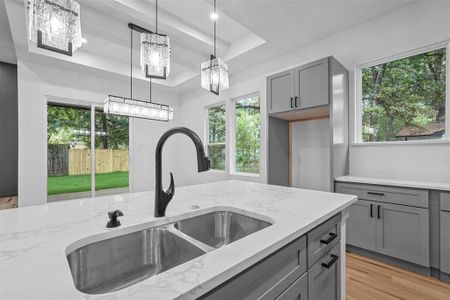 Kitchen with pendant lighting, light stone counters, sink, and a raised ceiling