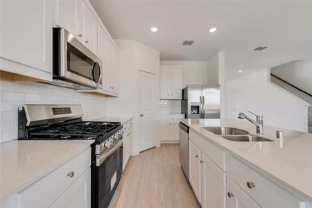 Kitchen featuring tasteful backsplash, white cabinetry, sink, light hardwood / wood-style floors, and stainless steel appliances