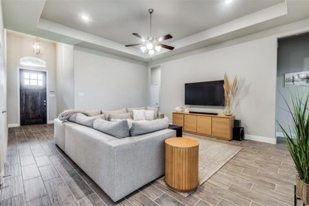 Living room with hardwood / wood-style flooring, ceiling fan, and a raised ceiling