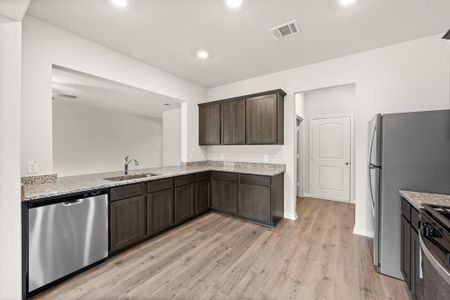 Kitchen with light hardwood / wood-style floors, dark brown cabinets, sink, light stone counters, and appliances with stainless steel finishes