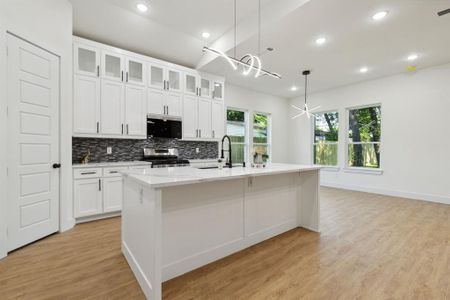 Kitchen featuring decorative light fixtures, an island with sink, sink, appliances with stainless steel finishes, and light hardwood / wood-style floors