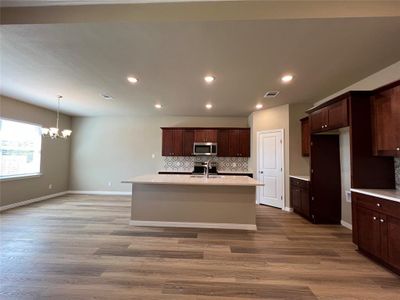 Kitchen with wood-type flooring, a chandelier, a kitchen island with sink, sink, and backsplash