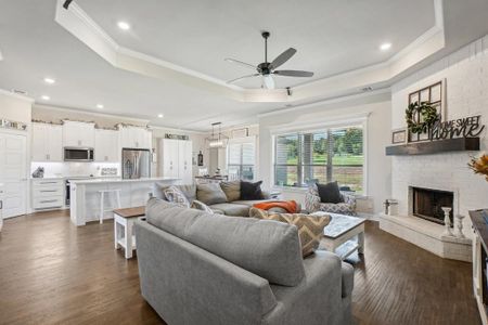 Living room featuring ceiling fan, a brick fireplace, a tray ceiling, crown molding, and dark hardwood / wood-style flooring