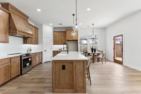 Kitchen featuring an island with sink, custom range hood, pendant lighting, light hardwood / wood-style flooring, and stainless steel electric range