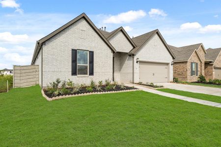 This is a single-story, modern brick home with a well-manicured lawn and an attached two-car garage. The house features a mix of white and earth-toned bricks, has a pitched roof with multiple gables, and a fenced backyard.