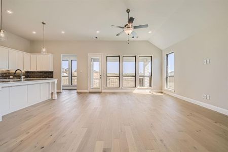 Unfurnished living room with ceiling fan, vaulted ceiling, light wood-type flooring, and sink