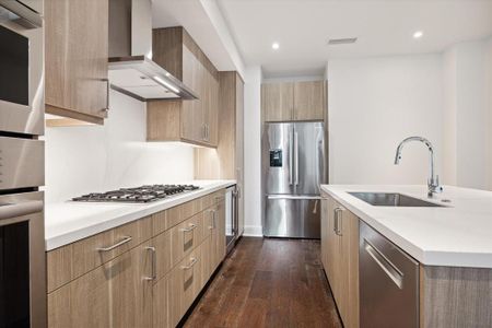 The kitchen features stainless steel Bosch appliances, sleek wooden cabinetry, a gas cooktop, quartz countertops and an undermount sink. The space is well-lit and has engineered hardwood flooring.