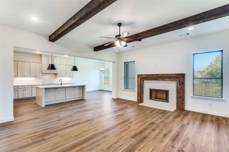 Unfurnished living room with light wood-type flooring, beam ceiling, sink, a tile fireplace, and ceiling fan