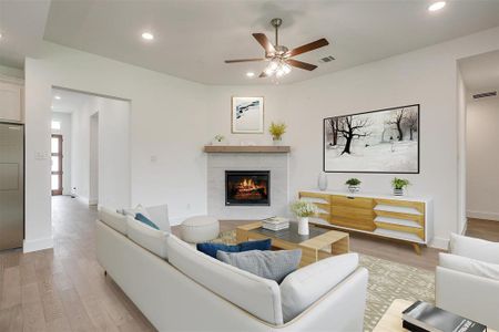 Living room with light hardwood / wood-style floors, a tiled fireplace, and ceiling fan