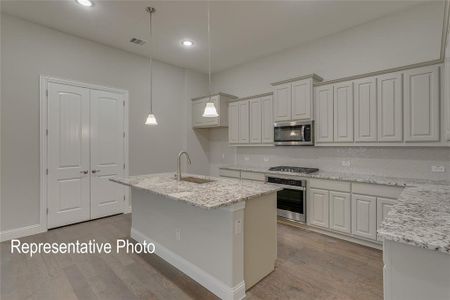 Kitchen with sink, stainless steel appliances, pendant lighting, light hardwood / wood-style flooring, and a center island with sink