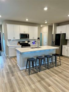 Kitchen featuring a center island with sink, light hardwood / wood-style floors, stainless steel appliances, sink, and white cabinets