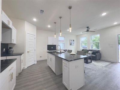 Kitchen featuring white cabinets, sink, ceiling fan, pendant lighting, and a kitchen island with sink