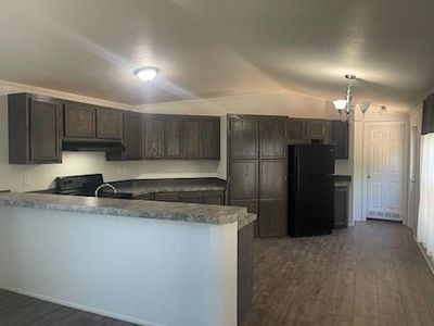 Kitchen with black appliances, kitchen peninsula, dark hardwood / wood-style floors, and dark brown cabinets