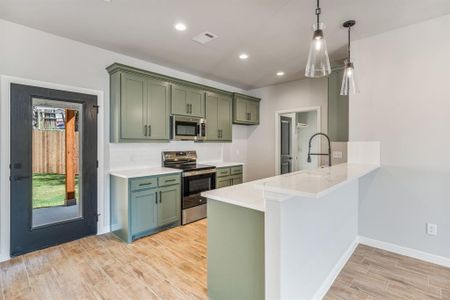 Kitchen with green cabinetry, appliances with stainless steel finishes, light wood-type flooring, and decorative light fixtures